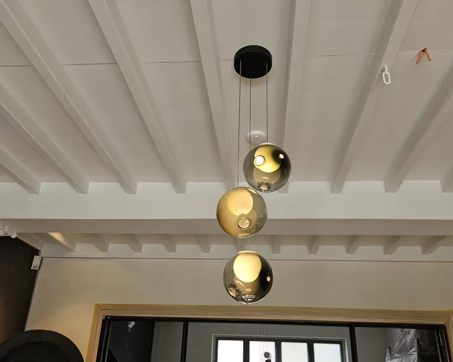 Drie glazen bolhanglampen onder een wit balkenplafond, in een woning in renovatie
