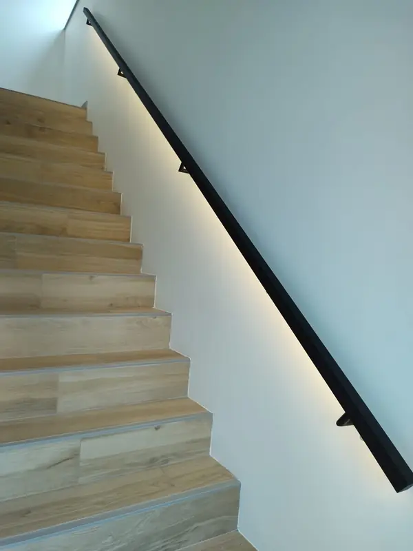 Houten trap met een zwarte leuning waaronder een ledstrip de treden verlicht