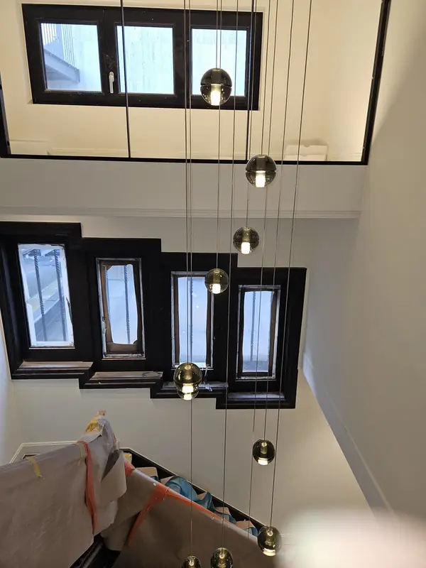 Glazen hanglampen op verschillende hoogtes in een hoge trappenhal met zwart omlijste ramen