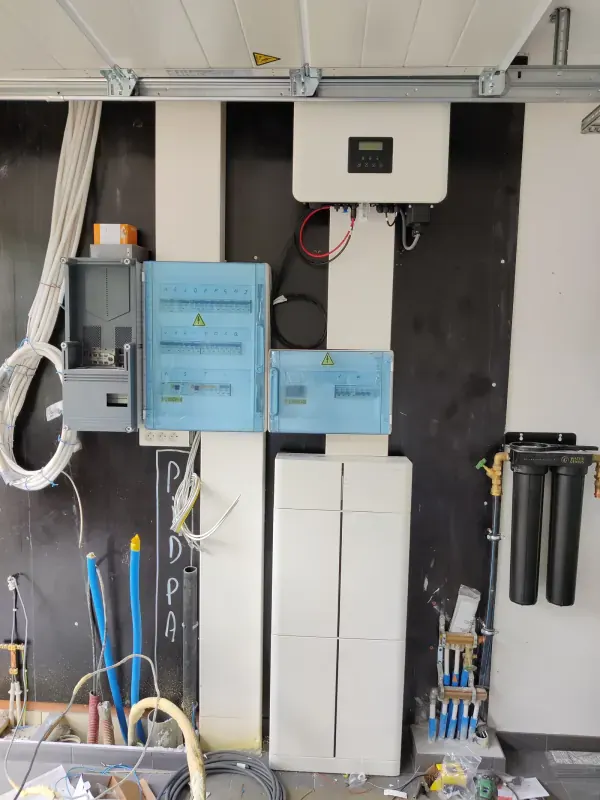 Technische wand in een garage met omvormer, witte batterijkasten en twee verdeelkasten