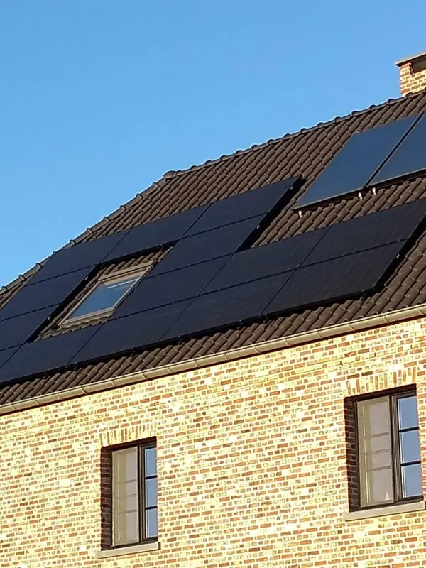 Zwarte zonnepanelen rond twee dakvensters op een woning van gele baksteen, onder een blauwe lucht